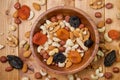 Natural nutritious mix of different nuts with dried apricots and plums in a wooden round plate on the brown wooden table. Mixture