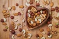 Natural nutritious mix of different nuts in a wooden plate of heart symbol shape on brown wooden table. Mixture of walnuts, huzeln