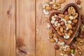 Natural nutritious mix of different nuts in a wooden plate of heart symbol shape on brown wooden table at the right side. Mixture