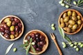 Natural olives in bowls with olive branch on black stone table top view.