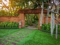 Natural orange clay brick arched wall entrance in a tropical garden with pattern of brown laterite walkway on green grass lawn