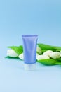 Vertical blank packaging cosmetic plastic bottle with fresh flowers on pastel blue background, close up mockup face cream