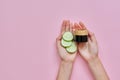 Woman& x27;s hands with glass bottle, cucumber slices on pink background