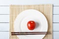 Natural organic tomato and food sticks on white plate. Wooden table with bamboo mat. Chinese and japanese kitchen concept. Top vie Royalty Free Stock Photo