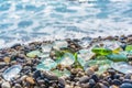 Natural polish textured sea glass and stones on the seashore. Azure clear sea water with waves. Green, blue shiny glass with multi