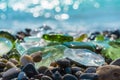Natural polish textured sea glass and stones on the seashore. Azure clear sea water with waves. Green, blue shiny glass with multi
