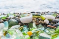 Natural polish textured sea glass and stones on the seashore. Azure clear sea water with waves. Green, blue shiny glass with