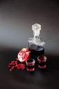 Natural pomegranate liqueur next to a ripe broken fruit and a handful of seeds on a black background