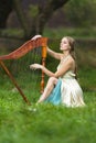 Natural portrait of sensual female harpist woman in light dress playing the harp in park outdoor