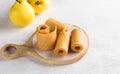 Natural quince pastille on a wooden board surrounded by fresh quince fruits on a light gray background