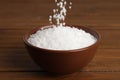 Natural sea salt falling into bowl on wooden table Royalty Free Stock Photo
