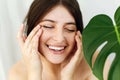 Natural Skin Care and Treatment. Portrait of beautiful young happy woman holding hands and massaging skin at green palm leaf. Girl Royalty Free Stock Photo