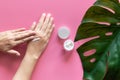 Natural skincare concept. woman apply white cream on her hands on pink background with jar of cosmetic cream