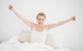 Natural smiling blonde sitting in bed and stretching her arms Royalty Free Stock Photo