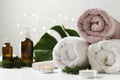 Natural spa procedures. Fresh tropical leaves, towels, candles and glass bottles of oil for body on the white surface against boke