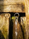 Natural village spring with clean drinking water. Water flows from an iron pipe from a wooden wall. Spring water glare Royalty Free Stock Photo