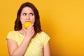 Natural vitamins and healthy food concept. Indoor shot of young brunette woman bits lemon with discontented facial expession,