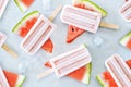 Natural watermelon juice popsicles with ice cubes over gray tray