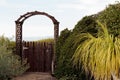Natural wood picket gate opens to distant view of opportunity or mystery, surrounded by green foliage
