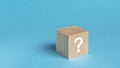 wooden toy cube with a question mark viewed high angle on a blue background with copy space in a conceptual image