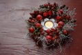Natural wreath with rose hips and small apples around a burning candle on a red wooden table, seasonal decoration in autumn, Royalty Free Stock Photo
