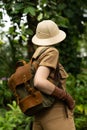Naturalist in khaki clothes, hat, leaver gloves with backpack walks in the rainforest surrounded by palms. Jungle tourist