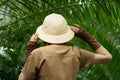 Naturalist in khaki clothes, hat, leaver gloves standing in the rainforest surrounded by palms. Jungle tourist