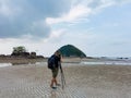 Nature photographer in the action. Alone traveller shoots the seascape with small island background on low tide sandy beach