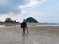 Nature photographer in the action. Alone traveller shoots the seascape with small island background on low tide sandy beach