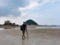 Nature photographer in the action. Alone traveller shoots the seascape with small island background on low tide sandy beach