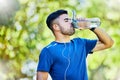 Nature, running and thirst, a man drinking water on fitness break with headphones in park. Health, exercise and freedom Royalty Free Stock Photo