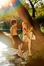 Naughty boy and girl sitting on a branch over water, laughing, having fun talking Royalty Free Stock Photo