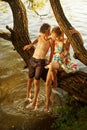Naughty boy and girl sitting on a branch over water, laughing, having fun talking Royalty Free Stock Photo