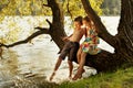 Naughty boy and girl sitting on a branch over water, laughing, having fun talking Royalty Free Stock Photo