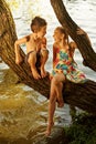 naughty boy and girl sitting on a branch over water, laughing out loud, having fun talking Royalty Free Stock Photo