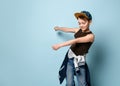 Naughty schoolboy in stylish cap jumping in place looking down under his feet with roguish smile.  isolated on blue background Royalty Free Stock Photo