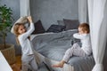 Naughty children a little boy and a girl in pajamas had a pillow fight on the bed in a gray bedroom. They like this game. Home is Royalty Free Stock Photo