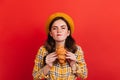 Naughty dark-haired girl bites her lip, wanting to eat delicious croissant. Lady in hat and yellow blouse posing on red Royalty Free Stock Photo