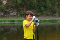 Naughty little kid standing on bank of mountain river holding digital camera he had just washed with soap. Half-length portrait,