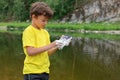 Naughty little kid standing on bank of mountain river holding smartphone he had just washed with soap. Half-length portrait, copy