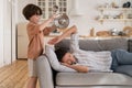 Naughty small kid rumbling kitchenware as stressed and tired mother sleeping on sofa in living room Royalty Free Stock Photo