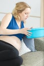 nauseous pregnant woman on sofa holding plastic bowl