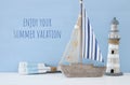 nautical concept with white decorative lighthouse, wooden oars and boat over blue background.