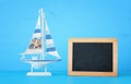 nautical concept with white decorative wooden boat next to empty blackboard for copy space over blue background. Royalty Free Stock Photo