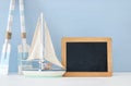 nautical concept with white decorative wooden oars and boat next to empty blackboard over blue background. Royalty Free Stock Photo