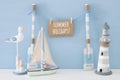 nautical concept with wooden decorative boat oars and hanging note message on a string next to lighthouse, seagull and boat over b