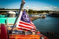 Nautical flag on back of teak wooden vintage speedboat in marina with docks and boats and retro motors in background - selective Royalty Free Stock Photo