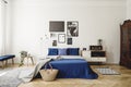 Navy blue bed with blanket next to cabinet with radio in retro bedroom interior with posters. Real photo Royalty Free Stock Photo