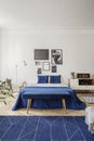 Navy blue bed and radio on cabinet in white bedroom interior with posters and carpet. Real photo