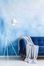 Navy blue couch with gray blanket and white standing lamp agains